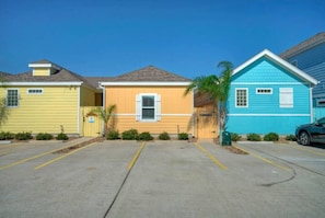 A row of colorful single-story buildings with a parking lot in front. - Sparkle Fish Private Breezeway Resort Pool (Port Aransas)