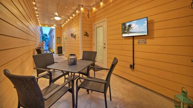 Eine Außenpatio mit Tisch und Stühlen, einem Deckenventilator, Lichterketten und einem an der Wand befestigten Fernseher.