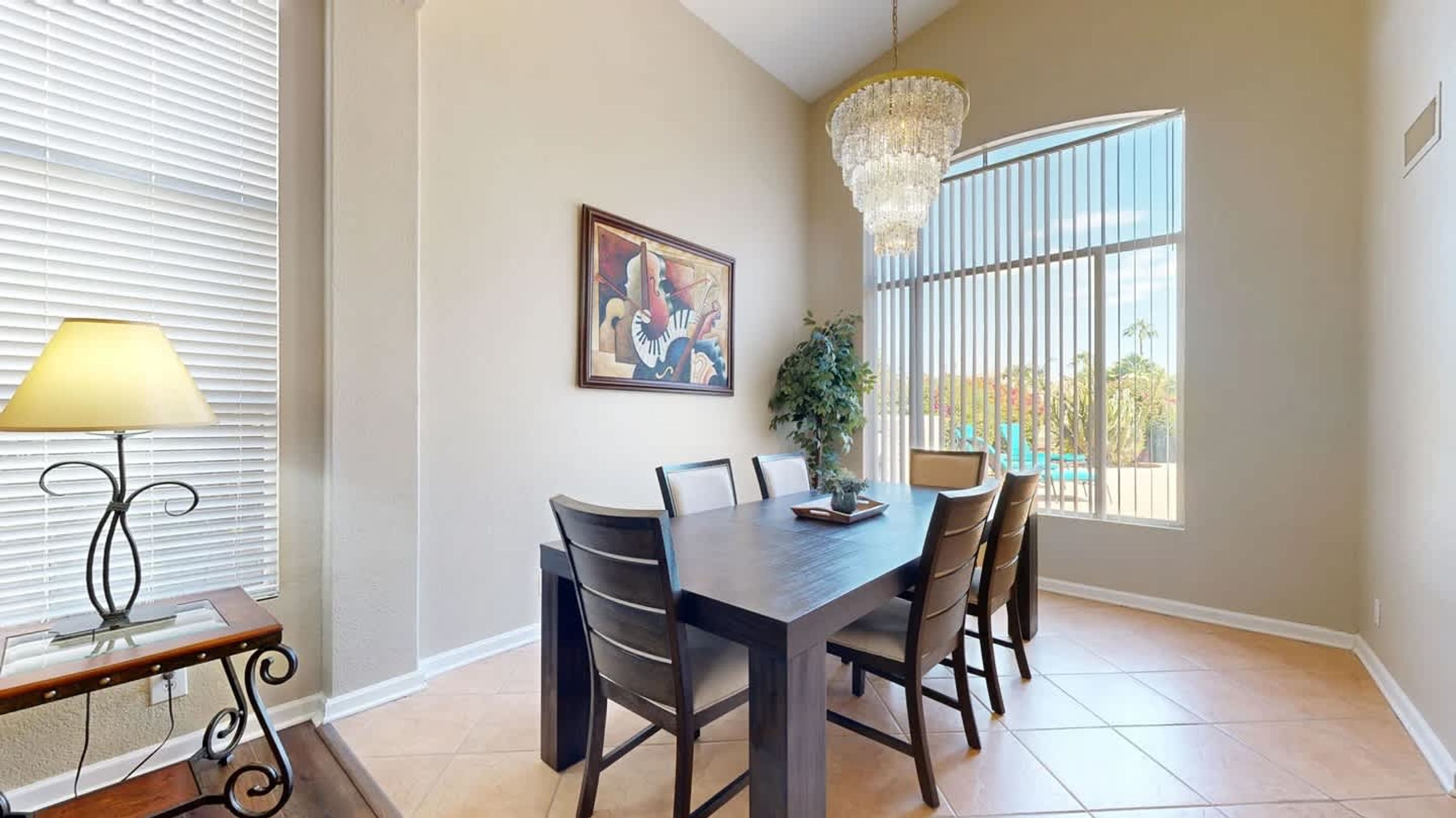 A dining area with a table, chairs, a chandelier, a lamp, and a window with blinds.