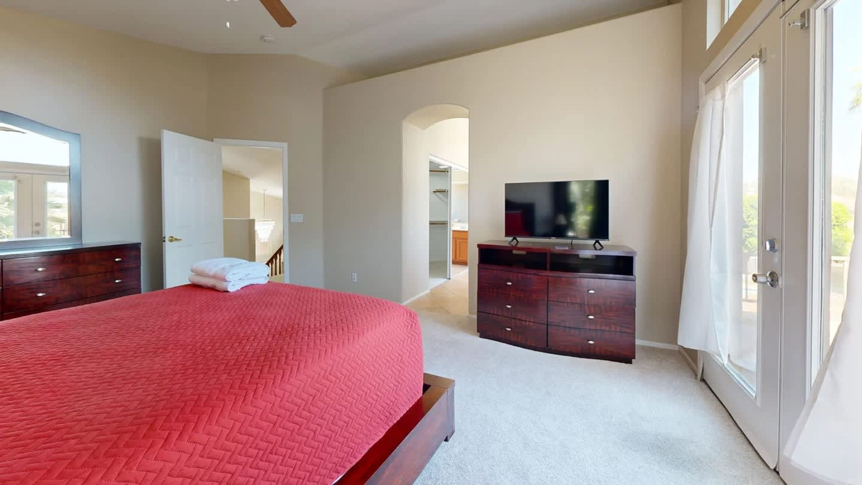 Ein Schlafzimmer mit einem großen Bett, einem Fernseher, einem Kleiderschrank und einer Tür zu einem anderen Raum.