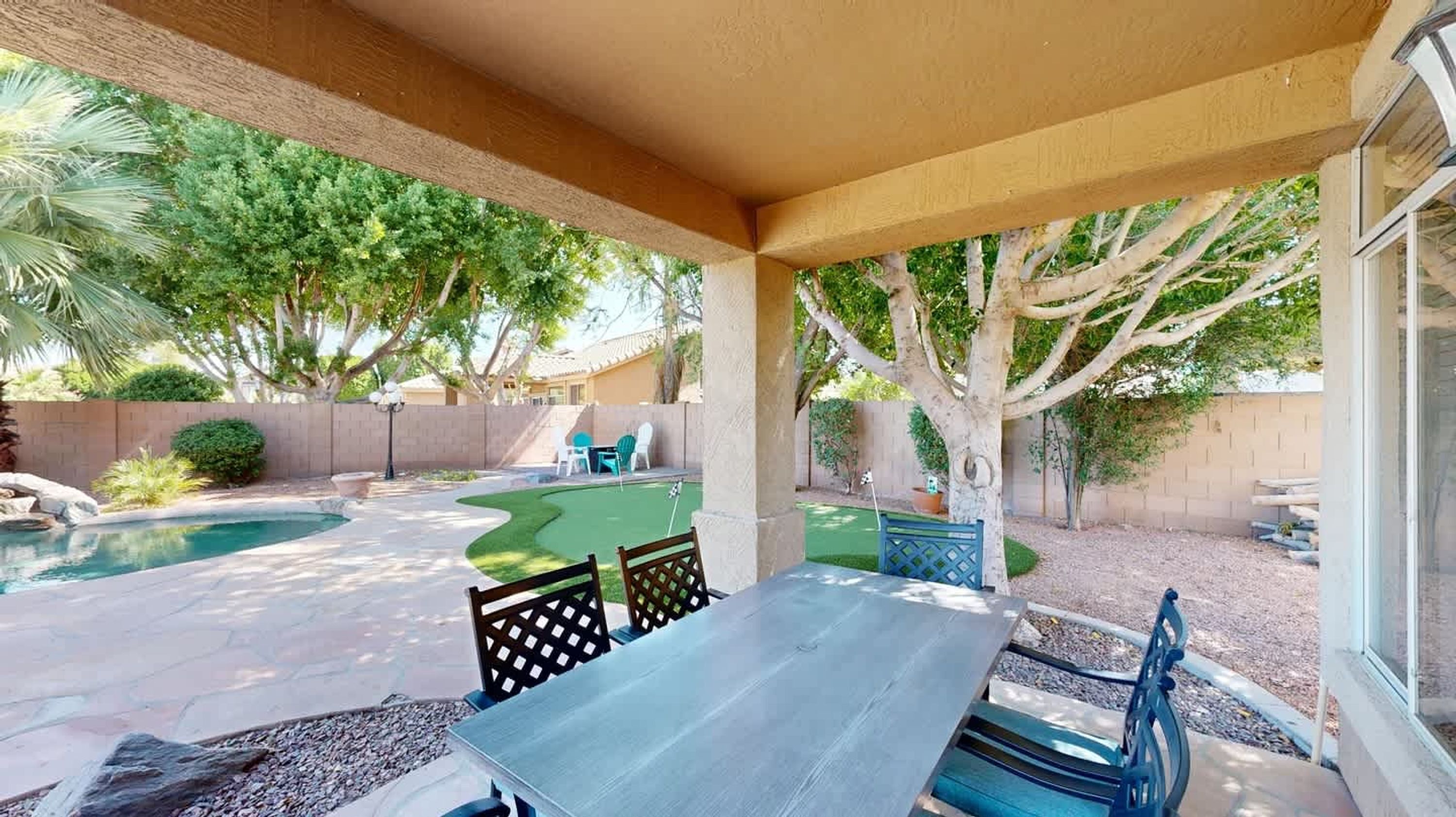 A covered patio with a pool, outdoor seating, and a tree.