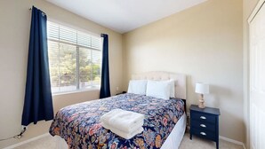 Quarto com uma cama, mesa de cabeceira, abajur e janela com cortinas.