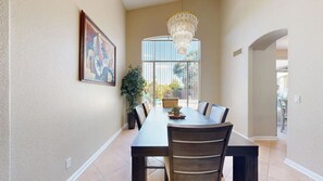A dining area with a long table, chairs, a chandelier, and a large window with a view. - Sleeps 10 Heated Pool Putt Putt Dogs Welcome (Chandler)