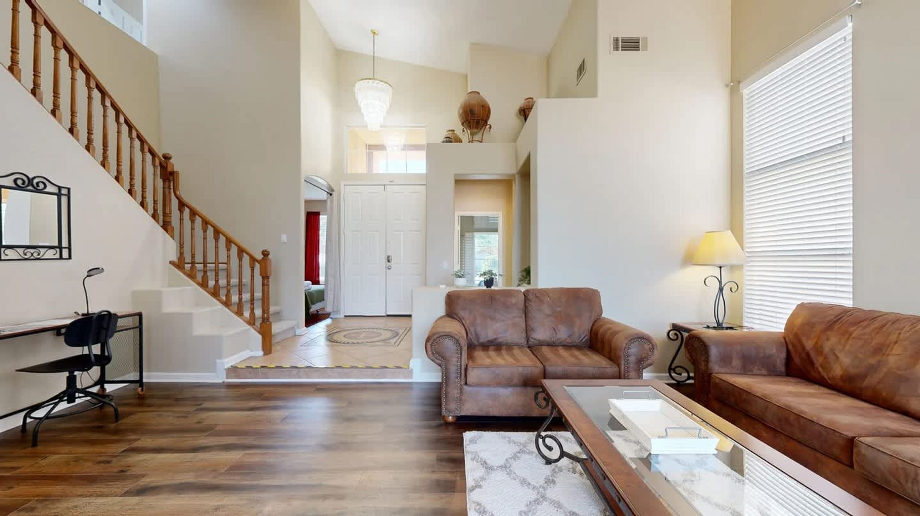 A spacious living room with a wooden staircase, leather sofas, a glass coffee table, and a dining area with a table and chairs.