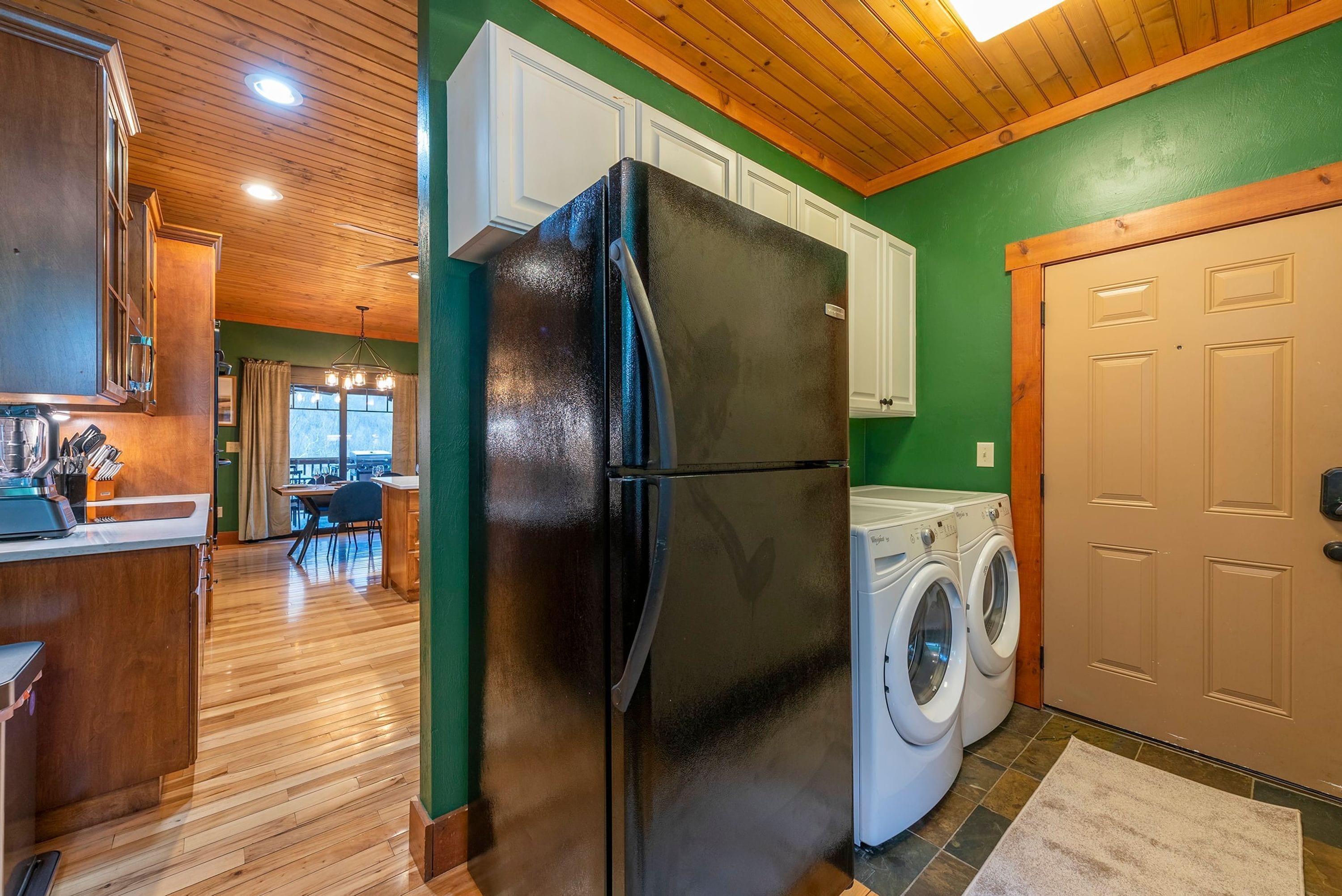 A kitchen with a refrigerator, washing machine, wooden cabinets, and a dining area with a table and chairs.