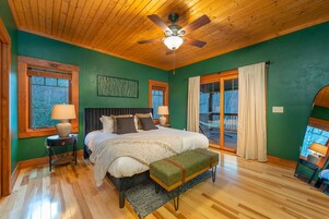 A bedroom with a large bed, two bedside tables, a ceiling fan, and a view of the outdoors through a sliding glass door.