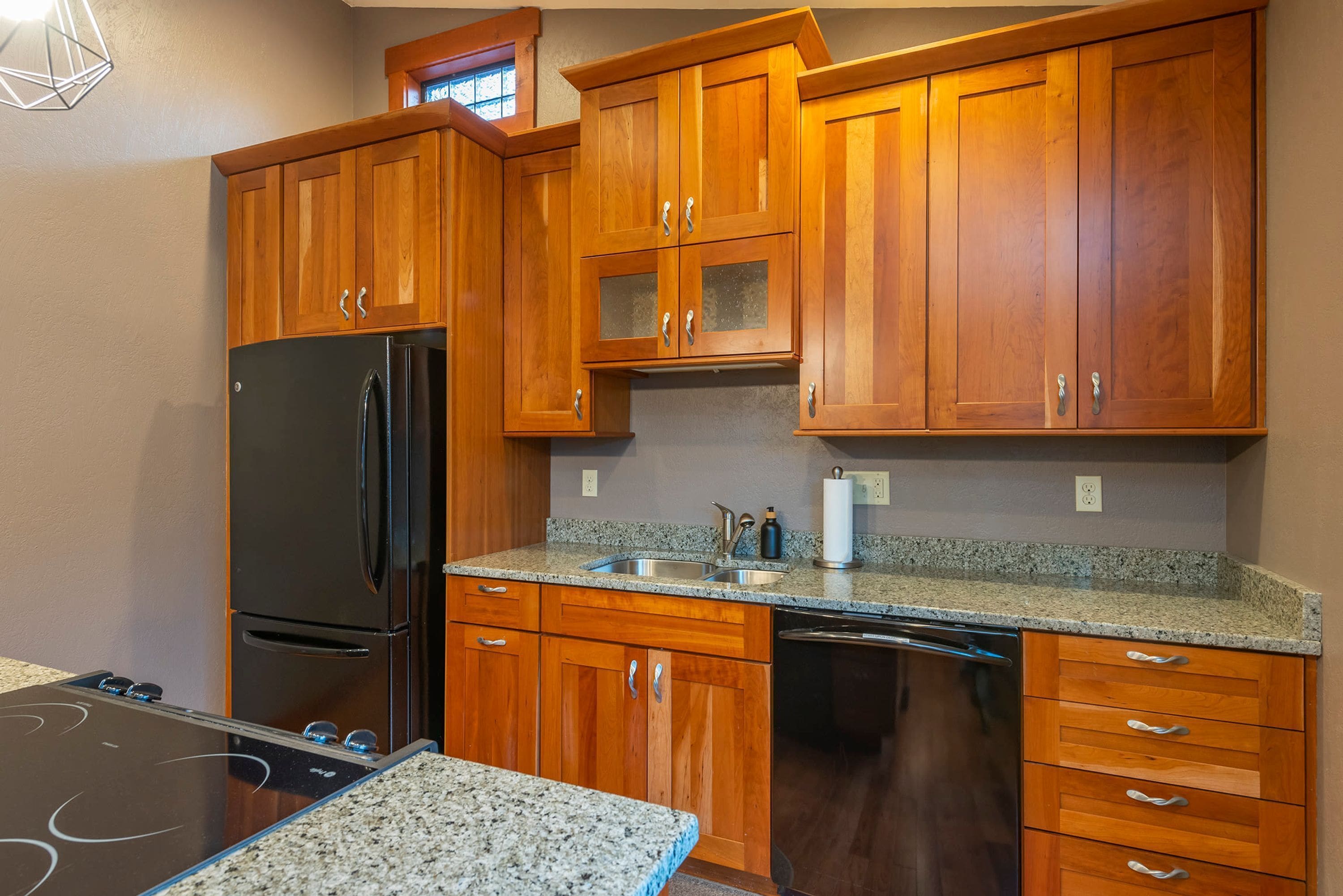 A kitchen with wooden cabinets, a black refrigerator, a dishwasher, and a granite countertop.