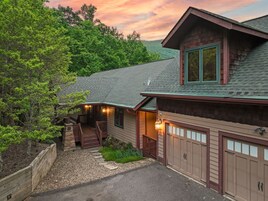 A two-story house with a covered porch, a garage, and a driveway leading to a wooden fence.
