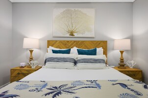 Una cama bien hecha con una colcha estampada, flanqueada por dos mesitas de noche con lámparas y adornos.