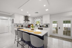 Une cuisine moderne avec des meubles blancs, un îlot central doté de tabourets et un pare-feu décoratif.