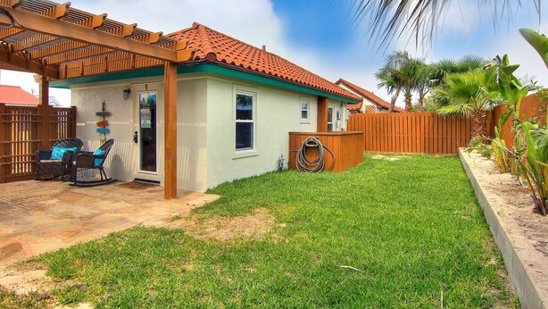 A single-story house with a tiled roof, a covered patio, and a fenced backyard. - Lorna Beach Cottage- Prime Location Pet Friendly (Port Aransas)