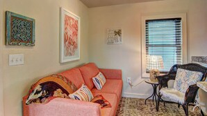 A cozy living room with a sofa, a chair, a window with blinds, and wall art. - Lorna Beach Cottage- Prime Location Pet Friendly (Port Aransas)