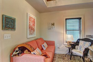 Ein gemütliches Wohnzimmer mit Sofa, Sessel, Fenster mit Jalousien und Wandbildern.
