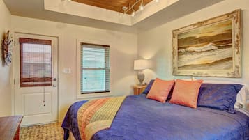 Un dormitorio con una cama grande, dos ventanas con persianas, un cuadro en la pared y techo de madera.