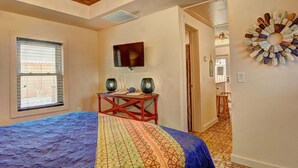 A bedroom with a bed, a television, a decorative wall piece, and a window with blinds. - Lorna Beach Cottage- Prime Location Pet Friendly (Port Aransas)