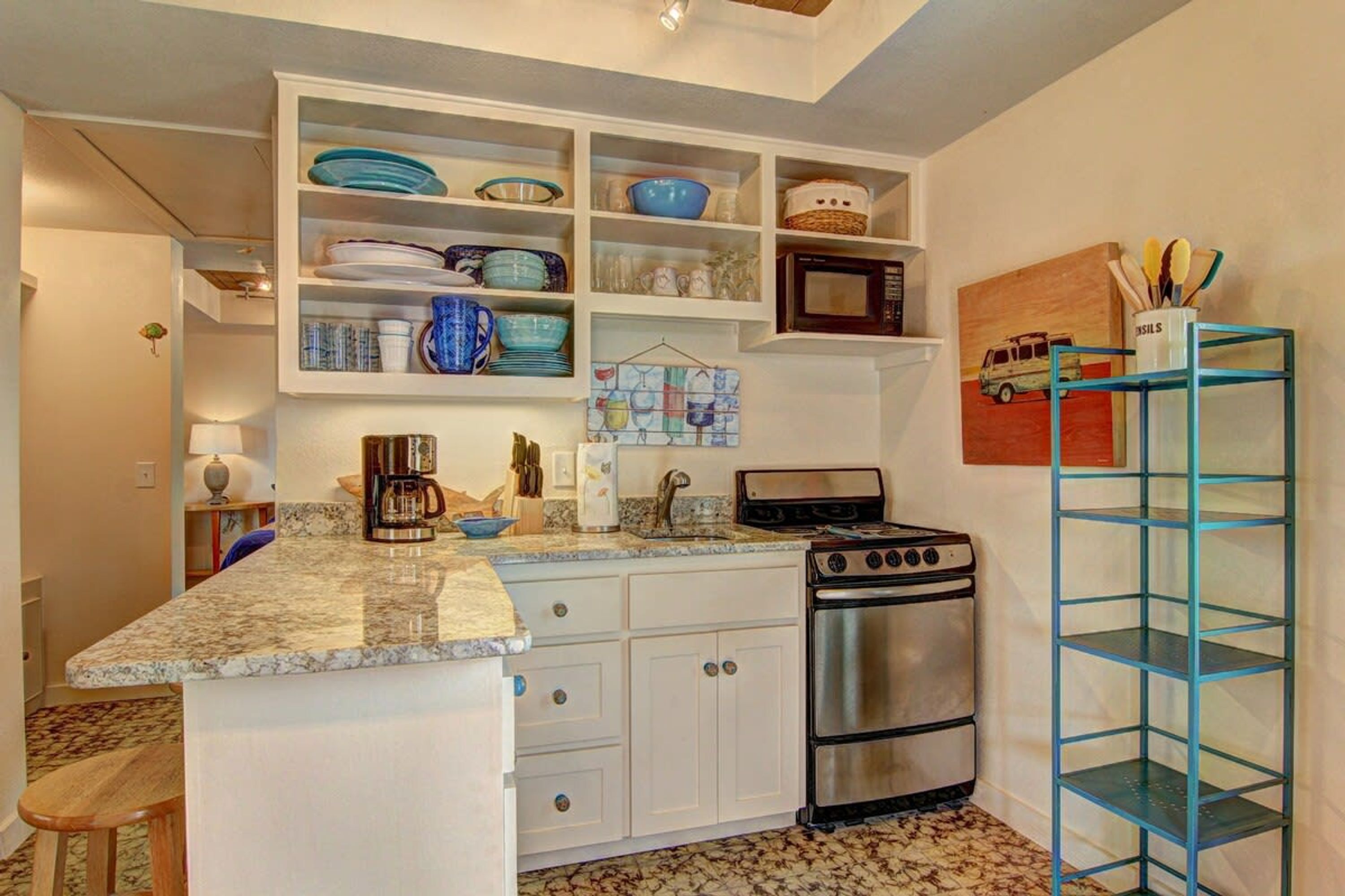 Una cocina compacta con muebles blancos, una estufa de acero inoxidable y un estante azul.