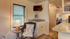 A kitchen with a built-in TV, a window with blinds, a chair, and a small table with a lamp. - Lorna Beach Cottage- Prime Location Pet Friendly (Port Aransas)
