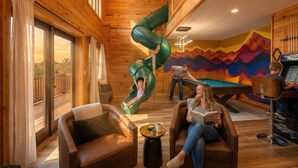 A cozy indoor space with a wooden interior, a green slide, a pool table, and a person reading a book. - The Summit in Mars Hill (Mars Hill)