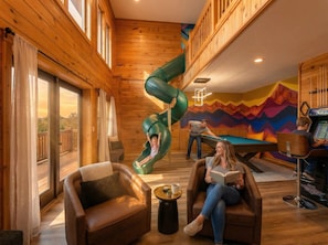 A cozy indoor space with a wooden interior, a green slide, a pool table, and a person reading a book. - The Summit in Mars Hill (Mars Hill)