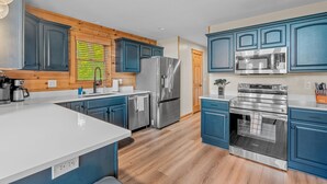 A modern kitchen with wooden paneling, blue cabinets, stainless steel appliances, and a large island. - The Summit in Mars Hill (Mars Hill)