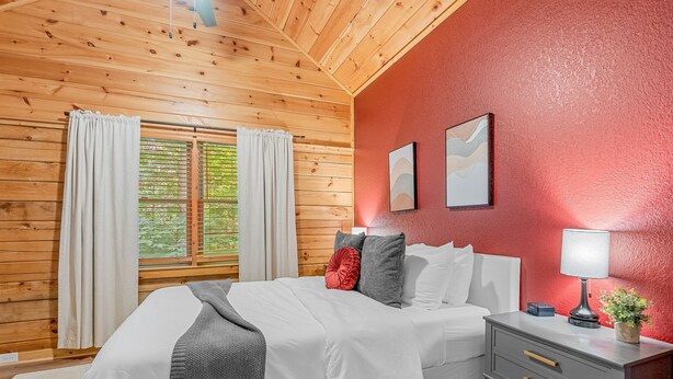 A bedroom with a wooden ceiling, a bed with white bedding, a nightstand with a lamp, and a red wall. - The Summit in Mars Hill (Mars Hill)