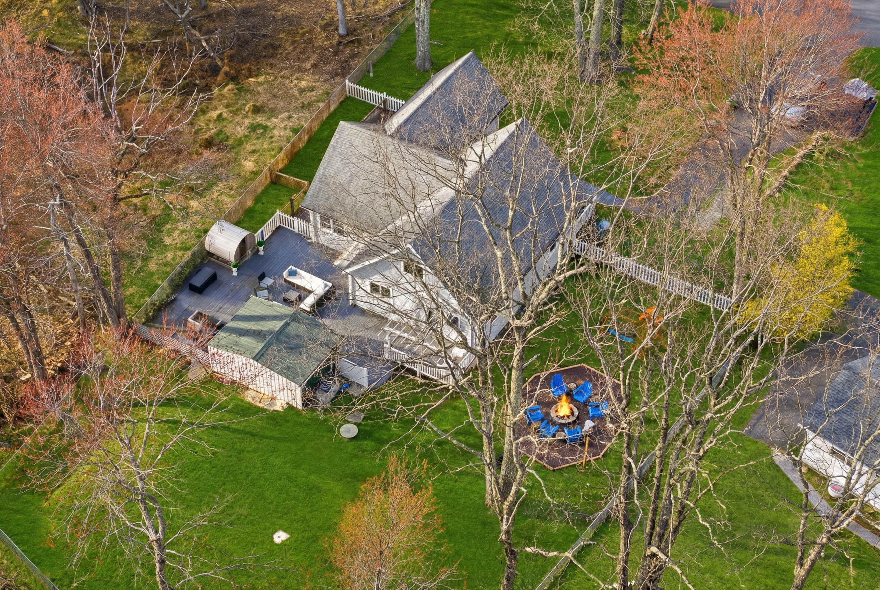 A large, two-story house with a sloped roof, surrounded by a fenced yard and trees.