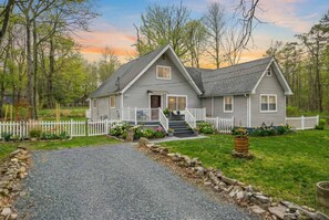 Ein zweistöckiges Haus mit einer Veranda, einem Steinweg, der zum Eingang führt, und einem umzäunten Garten.