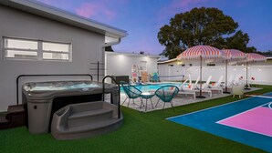 A backyard with a hot tub, a swimming pool, and lounge chairs under striped umbrellas. - Sports Court Playground Putt Putt Spa Pool (Bradenton)