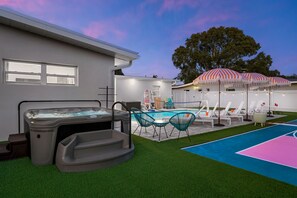 A backyard with a hot tub, a swimming pool, and lounge chairs under striped umbrellas. - Sports Court Playground Putt Putt Spa Pool (Bradenton)