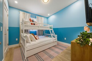 Dormitorio con literas de estructura blanca, un escritorio de madera y una planta.