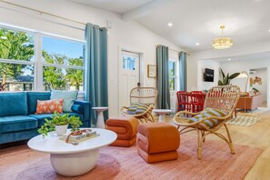 A modern living room with a blue sofa, wicker chairs, a coffee table, and a view of the outdoors. - Sports Court Playground Putt Putt Spa Pool (Bradenton)