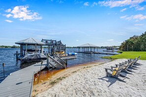 A waterfront property with a dock, a covered structure, and a sandy beach area with lounge chairs. - Luxury Lakefront Private Dock Pool In-ground Spa (Lake Placid)