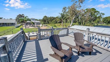 A wooden deck with Adirondack chairs, a pool, and a view of a house and landscape.