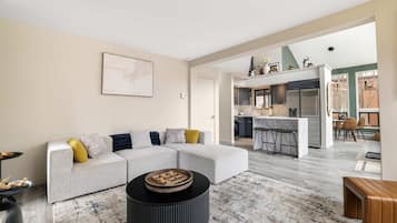 Una sala moderna con un sofá modular, una mesa de centro redonda y una cocina al fondo.