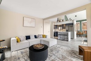 A modern living room with a sectional sofa, a round coffee table, and a kitchen in the background. - Pocono Escape Fire Pit Game Room Lake Access (East Stroudsburg)