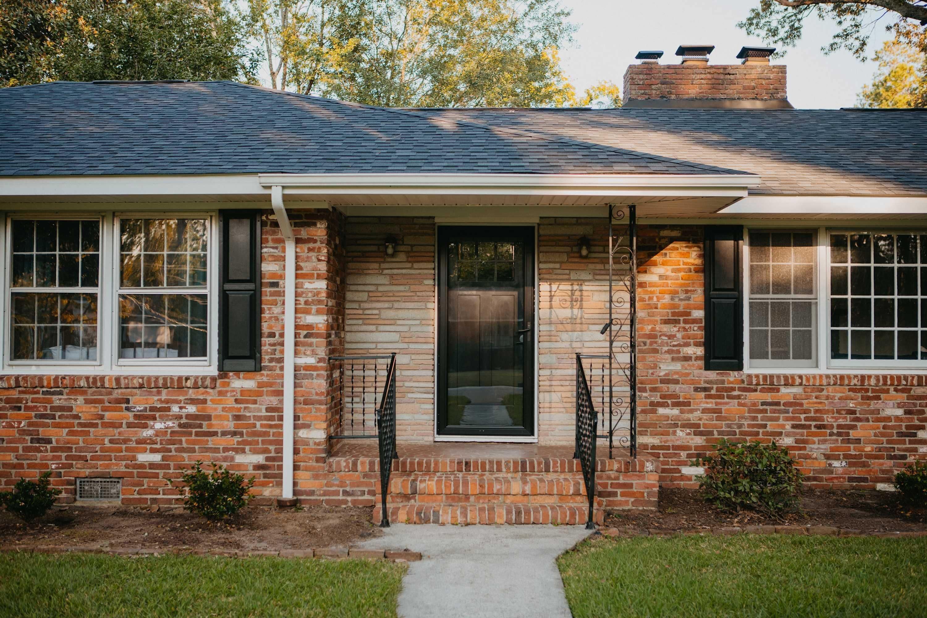A brick house with a front porch, a door, and windows.