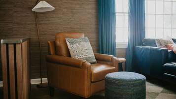 A room with a leather armchair, a floor lamp, a small ottoman, and a window with curtains.