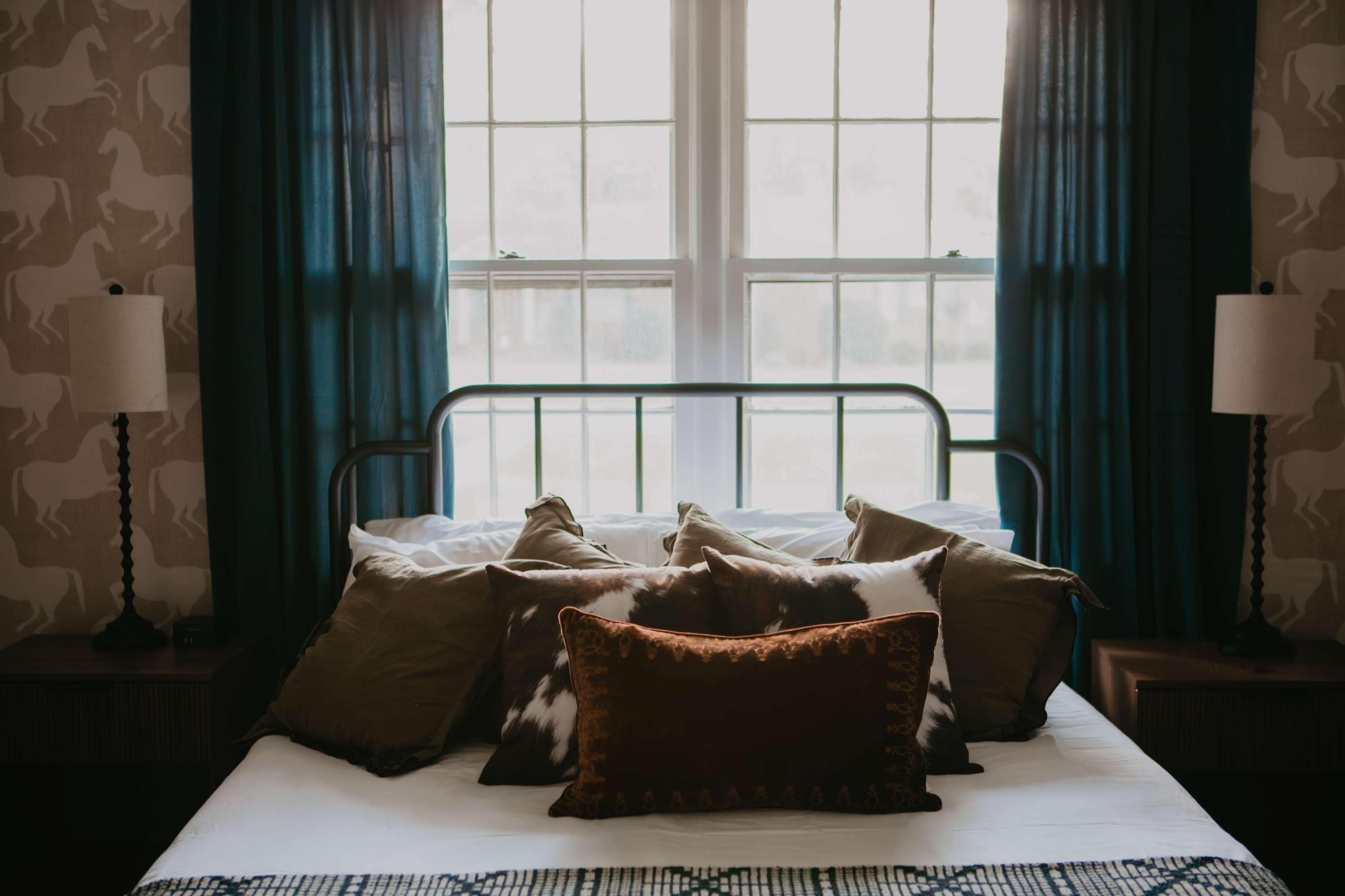 A bedroom with a bed, pillows, a window, curtains, and bedside lamps.