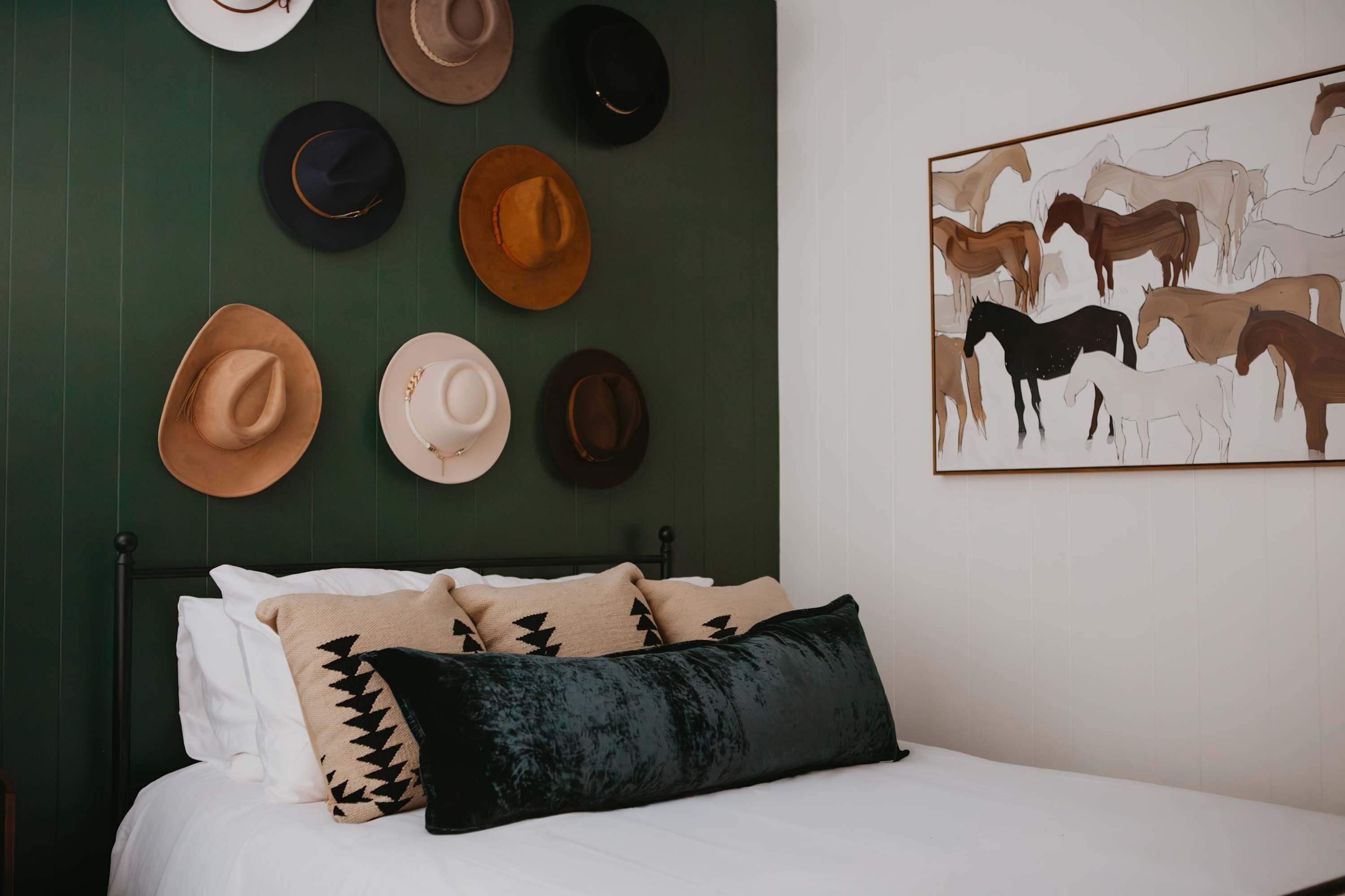 A bed with white bedding, a black pillow, and several hats hanging on the wall.