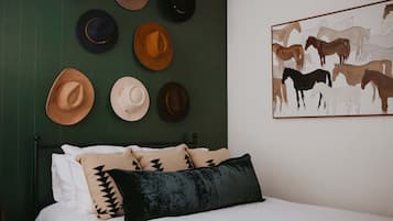 A bed with white bedding, a black pillow, and several hats hanging on the wall.
