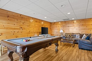 Ein Billardtisch mit Kugeln, eine Couch und ein Fernseher in einem Raum mit Holzwänden und Fliesen Decke.