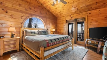 A wooden cabin bedroom with a bed, nightstands, a ceiling fan, and a large window.