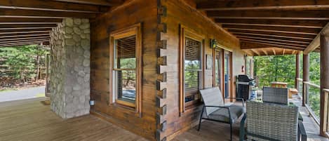 Eine Holzhütte mit Steinwand, großen Fenstern und einer Veranda mit Gartenmöbeln.