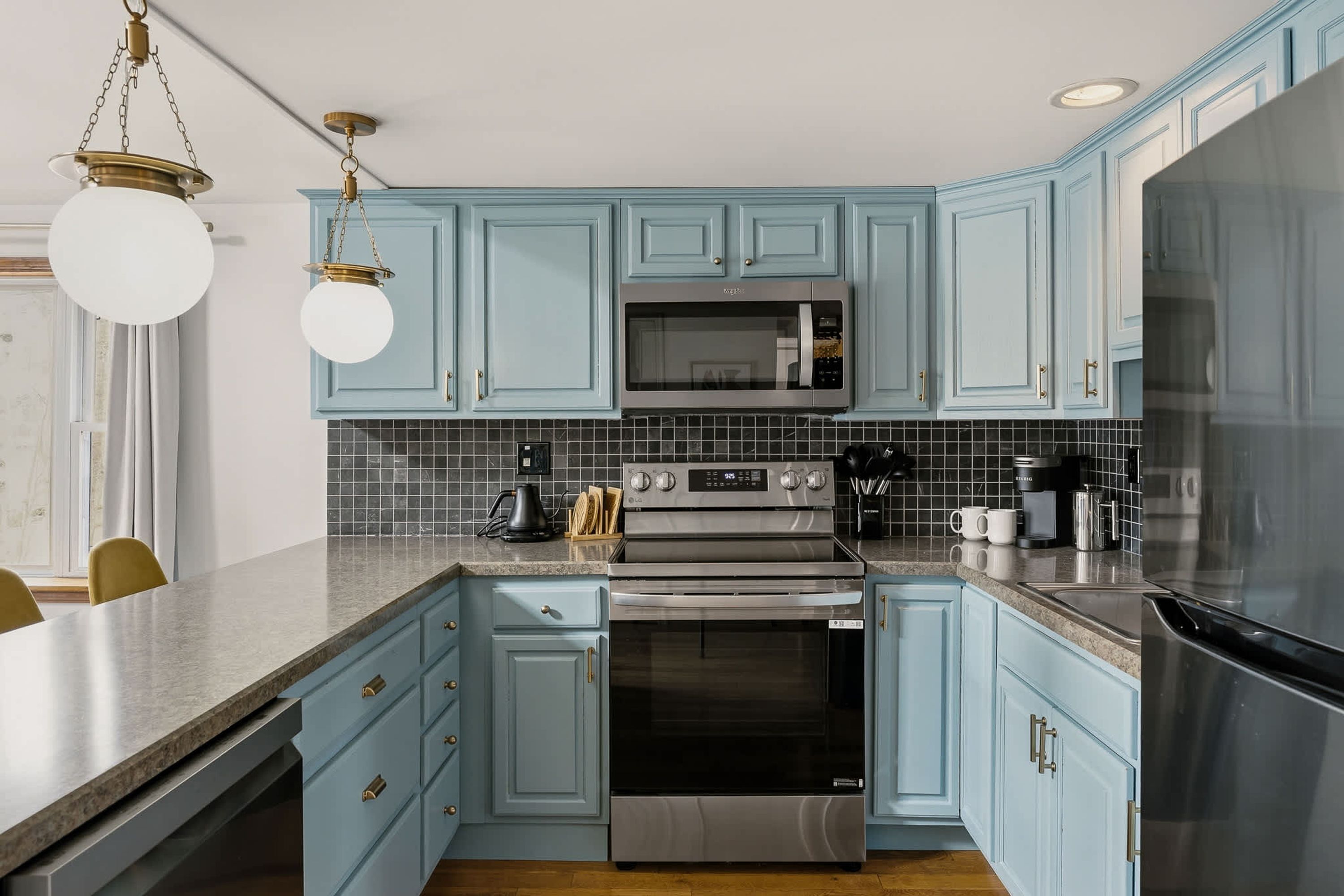 A kitchen with light blue cabinets, a stainless steel refrigerator, a microwave, an oven, and a coffee maker.