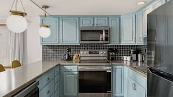 A kitchen with light blue cabinets, a stainless steel refrigerator, a microwave, an oven, and a coffee maker.