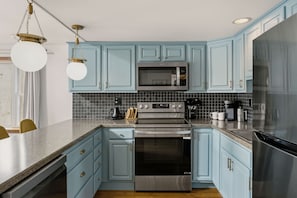 Una cocina con armarios azul claro, un refrigerador de acero inoxidable, un microondas, un horno y una cafetera.