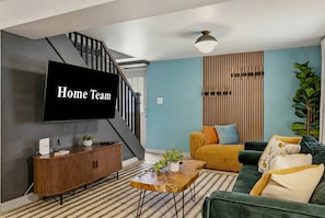 A modern living room with a staircase, a flat-screen TV, a wooden console, a sofa, and a coffee table.