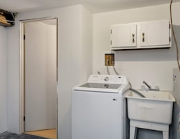A laundry room with a front-loading washer and dryer, a white cabinet above the dryer, and a door leading to another room.