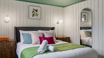 A neatly made bed with multiple pillows and a green throw blanket, a bedside table with a lamp, and a mirror on the wall.