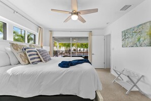 Ein Schlafzimmer mit Bett, Deckenventilator, Blick ins Freie und einem Bild an der Wand.